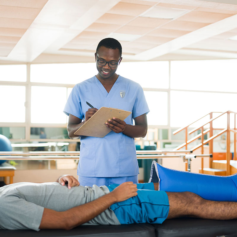 male occupational therapy assistant wearing scrubs helping patient laying down